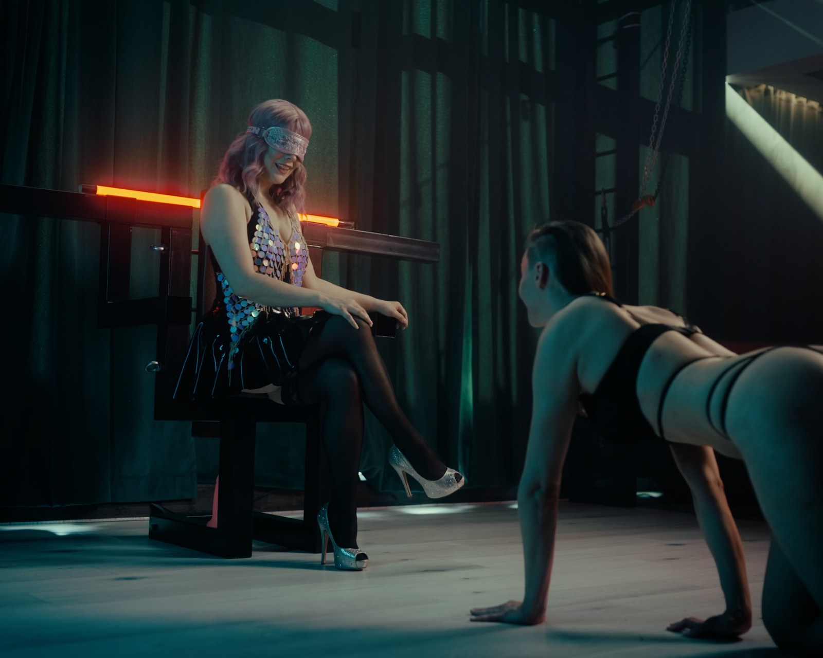 Devi Sparkles ja Jade alistumisen BDSM-kuvassa, jossa Jade ryömii Devi Sparklesin eteen hämärässä studiossa.