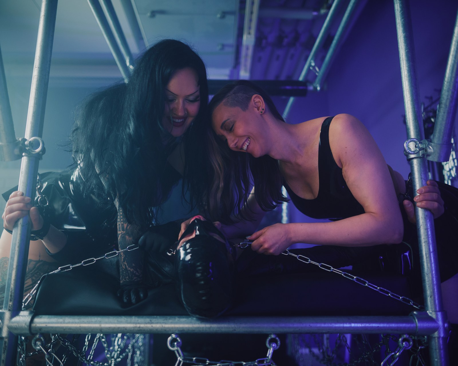 Miss Evilia ja lyhythiuksinen osallistuja hymyilevät metallisen kahlerakenteen äärellä.